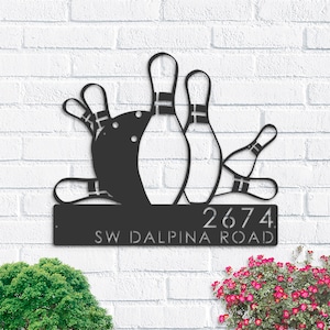 以下が含まれることがあります： ボウリングボールとピンをデザインした黒い金属製の家の番号札。札には「2674 SW DALPINA ROAD」と書いてあります。