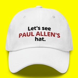 May include: White baseball cap with black text that reads "Let's see Paul Allen's hat."