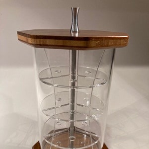 May include: A wooden and clear acrylic rotating display stand with three tiers. The stand has a hexagonal base and a silver metal top.