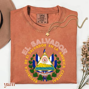 a red t-shirt with a graphic design of the Salvadoran flag, along with a necklace and some flowers.