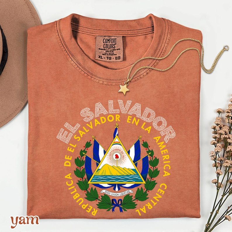 a red t-shirt with a graphic design of the Salvadoran flag, along with a necklace and some flowers.