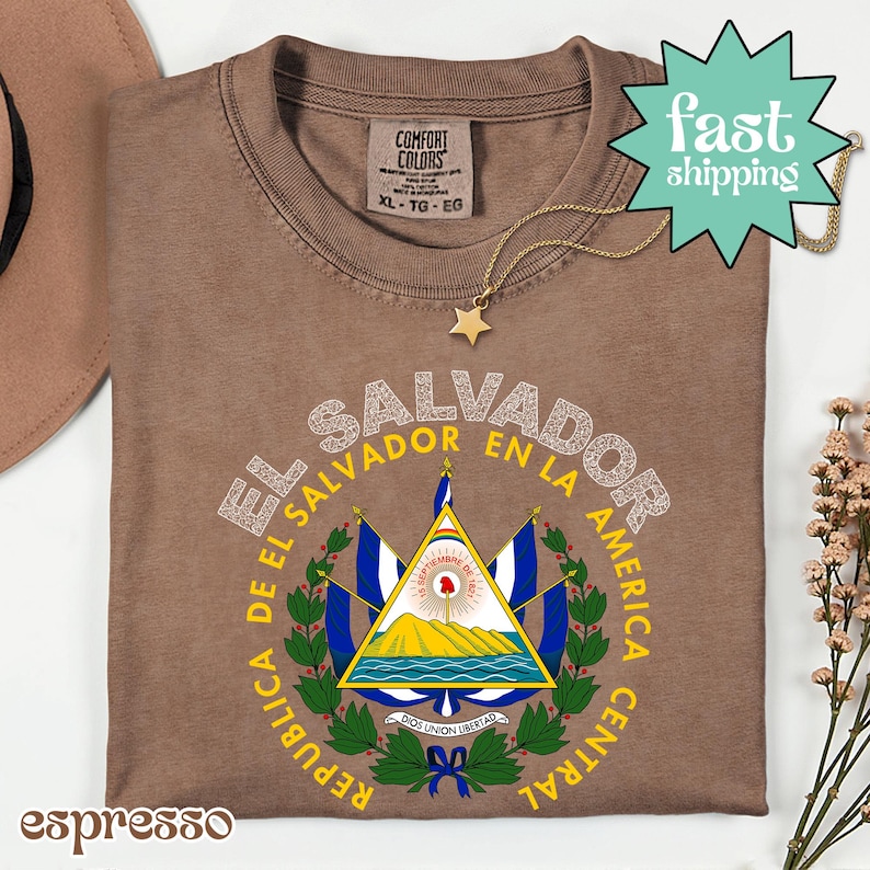 a brown t-shirt with a graphic design of the coat of arms of El Salvador, along with a star and a necklace.