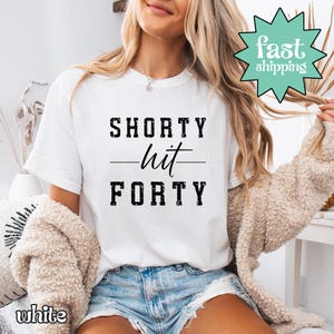 May include: White t-shirt with the text "SHORTY hit FORTY" in black block letters. The shirt has a crew neck and short sleeves. A green and white "fast shipping" graphic is visible in the upper right corner.