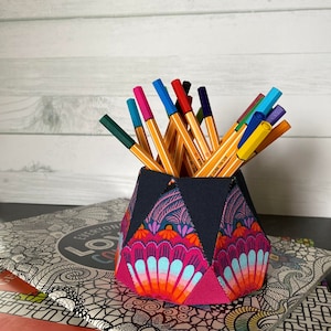 May include: A colorful fabric pencil holder with a geometric design. The holder is filled with a variety of colored pens and pencils.