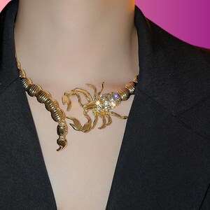 May include: A gold-tone necklace with a large scorpion pendant encrusted with clear rhinestones.