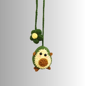 May include: A green crocheted avocado charm with a yellow flower and a brown pit, hanging from a green cord.