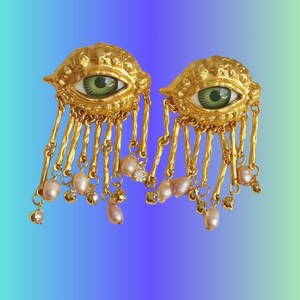 Puede incluir: Pendientes de ojo de oro con ojos verdes y perlas rosadas y cristales transparentes colgantes.