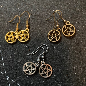Può includere: Tre paia di orecchini con un design a pentagramma. Un paio è dorato, un altro è argentato e l'ultimo è nero.