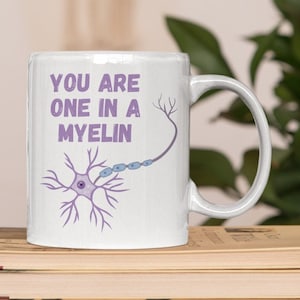 May include: White ceramic mug with a purple and blue illustration of a neuron and the text "You are one in a myelin".