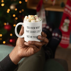 May include: White ceramic mug with black text that reads "You know what that sounds like? ... Not my problem." The mug is filled with hot chocolate and marshmallows.