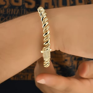 May include: A gold bracelet with a twisted rope design and a square clasp set with small clear stones.