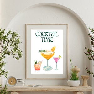 Puede incluir: Una impresión en acuarela enmarcada con tres cócteles. Las palabras "COCKTAIL TIME" están en verde en la parte superior. Los cócteles son naranja, rosa y rojo, cada uno con adornos. El marco es de color madera clara.