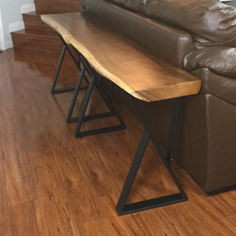 May include: A long, wooden console table with a live edge top and black metal legs. The table is made of natural wood with a rich brown color. The legs are made of sturdy metal and have a triangular shape.