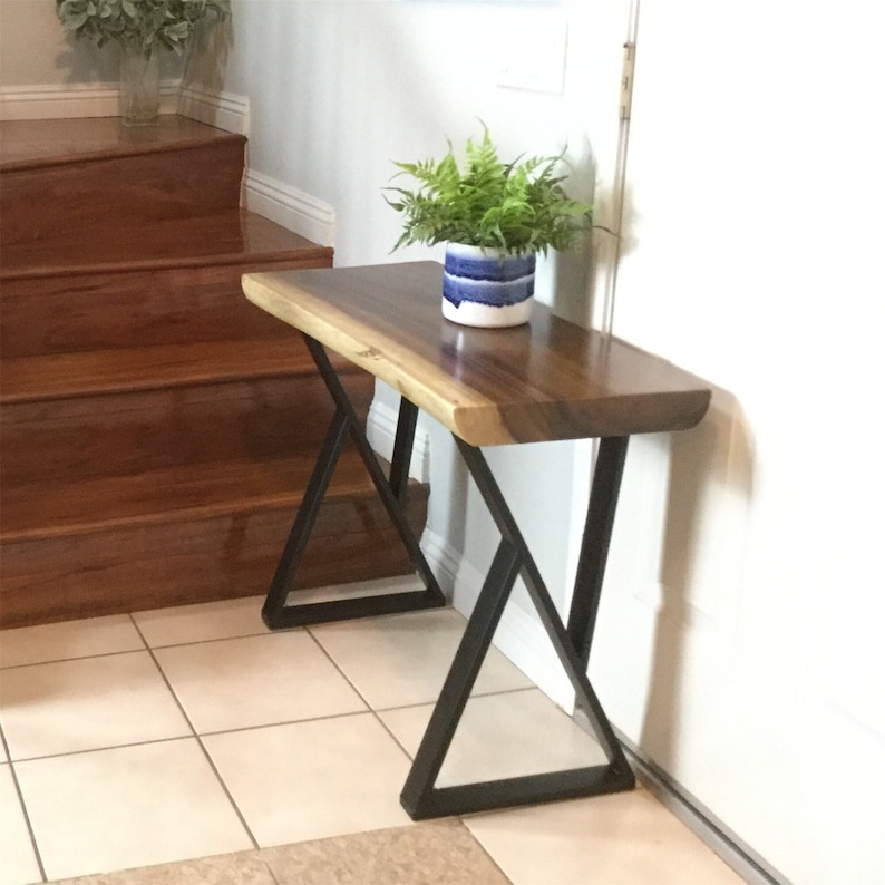 May include: A wooden console table with a live edge top and black metal legs. The table is in a home setting with a potted plant on top.