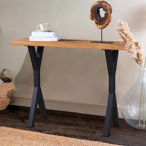 May include: A wooden console table with black metal legs. The table has a natural wood finish and the legs have a geometric design. The table is decorated with a wooden sculpture, a vase with dried flowers, and a stack of books.