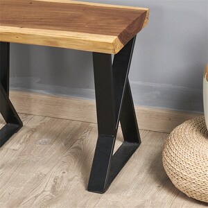 May include: A wooden bench with a natural wood top and black metal legs. The legs are in an X shape and the bench is sitting on a wooden floor.