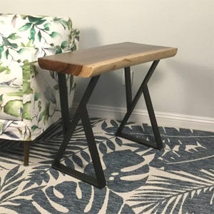 May include: A wooden end table with a live edge top and black metal legs. The table has a natural wood finish and the legs are in a geometric X shape.