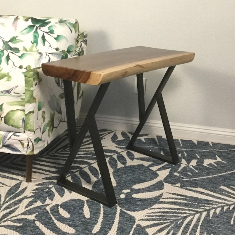 May include: A wooden end table with a live edge top and black metal legs. The table has a natural wood finish and the legs are in a geometric X shape.