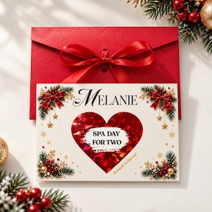 Könnte beinhalten: Eine rechteckige weiße Karte mit dem Namen Melanie, bedruckt mit einem großen roten Herz mit einer Rubbelfläche mit der Aufschrift SPA DAY FOR TWO, umgeben von Tannenzweigen, roten Schleifen, goldenen Sternen und einem roten Umschlag mit Schleife.