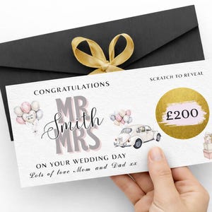 Könnte beinhalten: Eine Rubbelkarte zum Thema Hochzeit mit dem Text „Herzlichen Glückwunsch Mr & Mrs Smith zu Ihrem Hochzeitstag“. Die Karte zeigt Illustrationen von Luftballons, einem Oldtimer und Geschenken. Ein schwarzer Umschlag mit goldenem Band im Hintergrund.