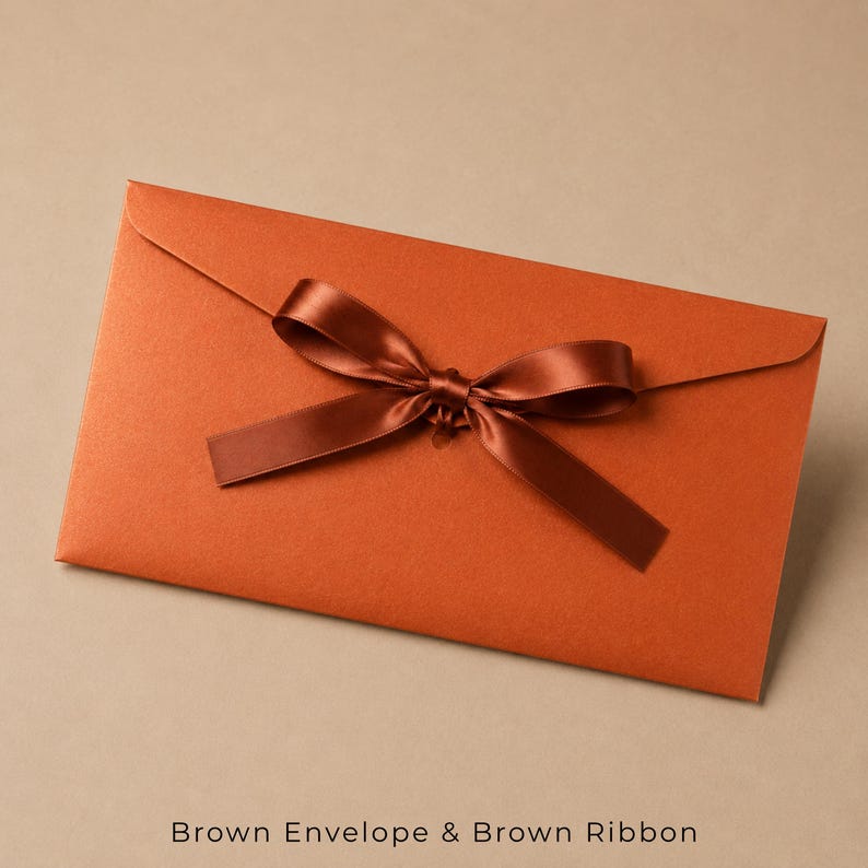 Op de afbeelding: Een rechthoekige, roestoranje envelop met een gladde, matte afwerking. Een donkerbruin satijnen lint is in een decoratieve strik over het midden van de envelopklep gebonden, wat een contrasterende textuur geeft aan het oranje papier.