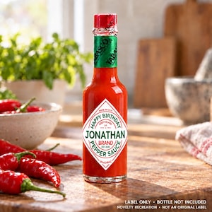 Puede incluir: Una botella de vidrio de salsa de chile rojo con una etiqueta blanca en forma de diamante que dice Happy Birthday Jonathan Brand Est. 2026. La botella tiene una tapa roja y una banda verde en el cuello. El volumen es de 148 ml.