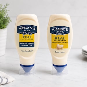 Puede incluir: Dos botellas de mayonesa con etiquetas personalizadas. La botella de la izquierda dice MEGAN'S EST.2025 REAL MAYONNAISE HAPPY 60TH BIRTHDAY Love from John. La botella de la derecha dice AIMEE'S EST.2025 REAL MAYONNAISE HAPPY BIRTHDAY! From James.