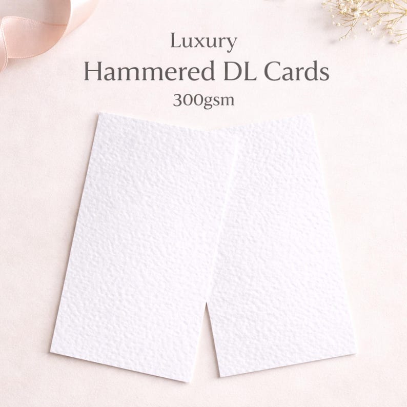 May include: Two white, textured DL cards with the text "Luxury Hammered DL Cards 300gsm". The cards are rectangular and have a hammered paper texture. The background is a soft, neutral colour.