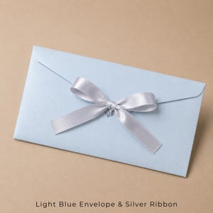 Op de afbeelding: Een lichtblauwe rechthoekige envelop met een gladde, matte afwerking. In het midden van de klep aan de voorzijde bevindt zich een decoratief zilverkleurig satijnen lint dat is gestrikt tot een nette strik. De envelop ligt horizontaal.