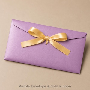 Op de afbeelding: Een rechthoekige lavendelkleurige envelop met een glinsterende afwerking, voorzien van een centraal geplaatst gouden satijnen lint gestrikt tot een strik. De envelopflap wordt vastgehouden door het lint dat door een opening gaat.