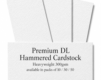 Könnte beinhalten: Drei Bögen weißer, strukturierter Karton, die fächerförmig angeordnet sind. Ein rechteckiges Etikett im Vordergrund zeigt den schwarzen Text: Premium DL Hammered Cardstock, Heavyweight 300gsm, available in packs of 10 / 30 / 50.