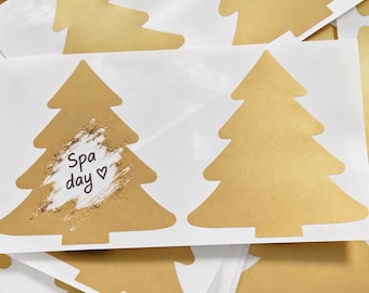 Könnte beinhalten: Ein Bogen mit goldfarbenen Aufklebern in Form von Weihnachtsbäumen. Ein Aufkleber zeigt einen weißen, strukturierten Bereich mit dem Text "Spa day" und einem kleinen Herzsymbol in Schwarz. Die anderen Aufkleber sind einfarbig gold.