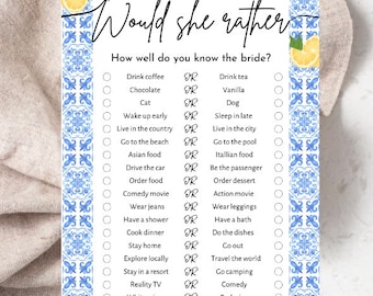 May include: A white game card with the text "Would she rather" in elegant script. The card features a blue and white tile design and lemon illustrations. The game includes questions like "Drink coffee or Drink tea?" and "Diamonds or Pearls?"