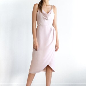 May include: A light pink midi dress with a cowl neck and thin straps. The dress has a wrap-style skirt and a fitted bodice.
