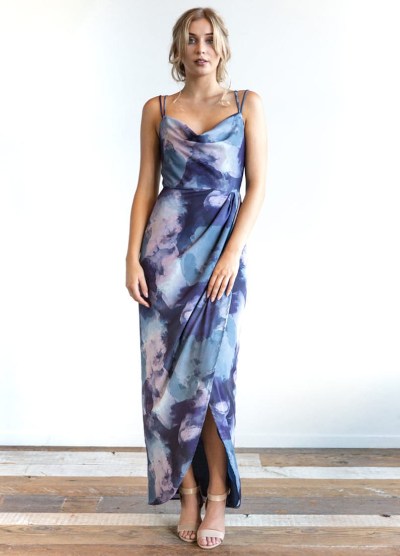 May include: A long, blue and purple floral print maxi dress with a cowl neck and a side slit. The dress has thin straps and a fitted bodice.
