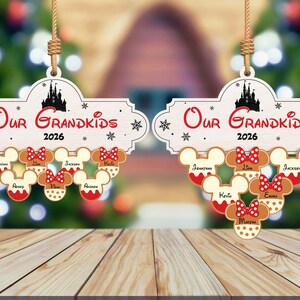 May include: Two wooden Christmas ornaments with the text "Our Grandkids 2026". Each ornament features Mickey Mouse head-shaped cookies with names and red bows. A black castle silhouette is at the top.