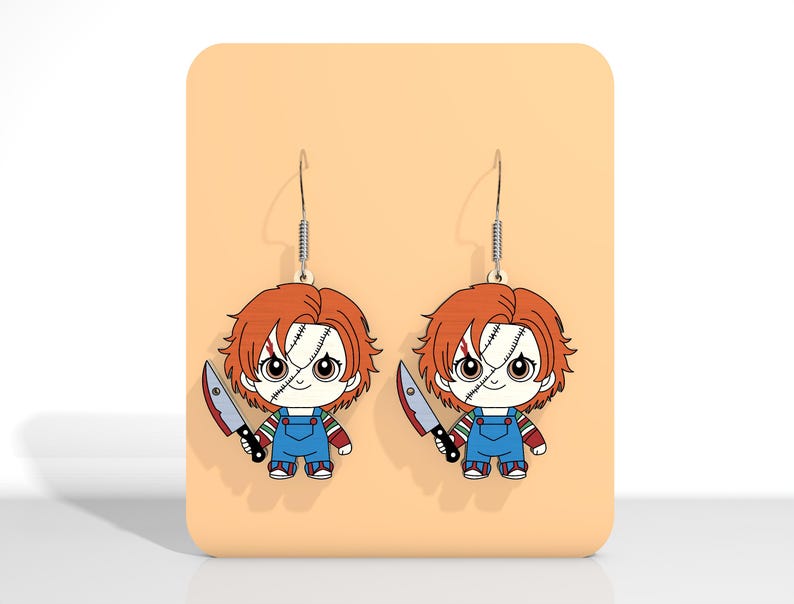 May include: A pair of dangle earrings featuring a cartoon Chucky doll design. Each earring depicts Chucky with red hair, blue overalls, and a knife. The earrings hang from silver-colored fish hooks.