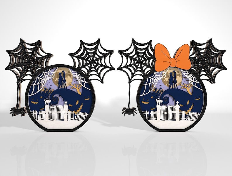 K&ouml;nnte beinhalten: Zwei Halloween-Dekorationen in Form von M&auml;useohren. Eine hat ein schwarzes Spinnennetz-Design und die andere eine orangefarbene Schleife. Jede zeigt eine mehrschichtige Szene mit Vollmond, Silhouetten und einer gruseligen Landschaft.