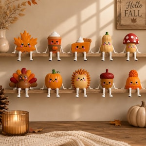 May include: A collection of ten small, decorative autumn-themed figurines with smiling faces and dangling legs, arranged on two wooden shelves. The figures include a maple leaf, coffee cup, pumpkin pie, squash, mushroom, turkey, pumpkin, hedgehog, acorn, and knit hat.