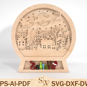 May include: A wooden snow globe with a laser cut design of a winter village scene with Santa flying overhead. The base of the snow globe has the word "Believe" written in colourful letters.