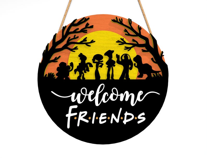 Pu&ograve; includere: Un cartello rotondo in legno con sagome nere di personaggi dei cartoni animati su uno sfondo di tramonto arancione e giallo. Il cartello recita "welcome FRIENDS" in scrittura bianca. Una corda marrone &egrave; attaccata per appenderlo.
