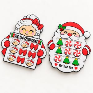 Puede incluir: Dos tableros de juego tres en raya de silicona con forma de Santa Claus y la Señora Claus. El tablero de la Señora Claus incluye el texto TIC-TAC CHRISTMAS con piezas en forma de lazos y caras. El tablero de Santa incluye el texto Tic Tac Toe con árboles y caramelos.