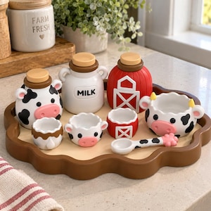 May include: A ceramic breakfast set on a brown scalloped tray featuring a cow-shaped creamer, a milk jug labeled MILK, a red barn-shaped container, two small cow-themed bowls, a small brown and white bowl, and a cow-patterned spoon with a hoof handle.