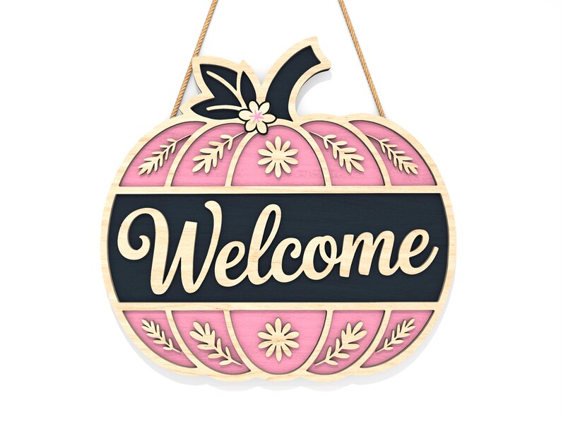 May include: A wooden pumpkin-shaped welcome sign with a pink interior and a black banner that reads "Welcome". The sign has a natural wood border and is decorated with floral and leaf cutouts. It hangs from a natural fiber rope.