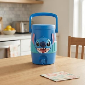 May include: A blue plastic beverage cooler featuring a molded 3D Stitch character face on the front. The cooler has a top handle, a light blue textured band around the middle, and a small dispensing spigot located at the bottom center of the unit.