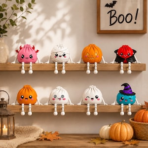 May include: Eight small, round, cartoon-style figurines with dangling articulated legs arranged on two wooden shelves. The characters feature various Halloween-themed designs including a pink devil, a white mummy, a pumpkin, a vampire, and a witch.