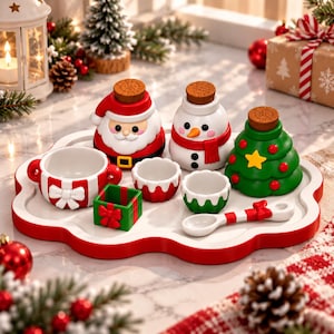 May include: A festive ceramic set on a white scalloped tray featuring a Santa Claus jar, a snowman jar, a Christmas tree jar, a gift-shaped box, a bowl with a bow, two small cups, and a spoon with a red and white striped handle and bow.