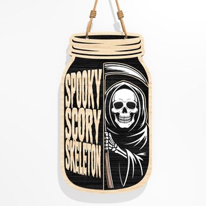 Puede incluir: Cartel de Halloween de madera con forma de tarro. El cartel presenta las palabras "Spooky Scary Skeleton" en vertical. Una ilustraci&oacute;n en blanco y negro de la Parca est&aacute; a la derecha. Una cuerda de yute est&aacute; unida para colgarlo.