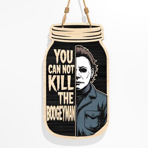 Puede incluir: Cartel de madera con forma de tarro con el texto "YOU CAN NOT KILL THE BOOGEYMAN" y un gr&aacute;fico de un personaje enmascarado. El cartel es negro con un borde de madera clara y una cuerda de yute para colgar.