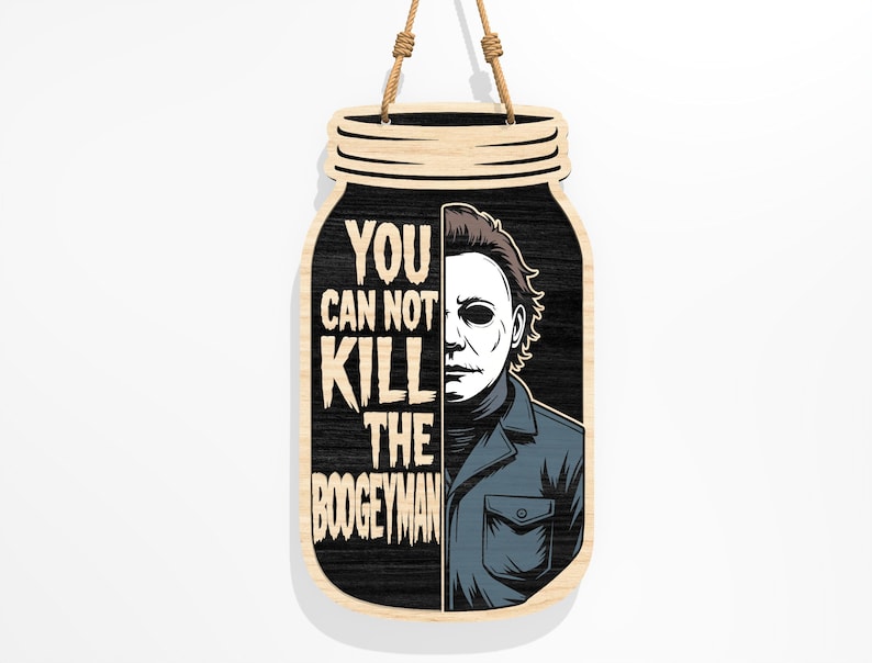 Puede incluir: Cartel de madera con forma de tarro con el texto "YOU CAN NOT KILL THE BOOGEYMAN" y un gr&aacute;fico de un personaje enmascarado. El cartel es negro con un borde de madera clara y una cuerda de yute para colgar.